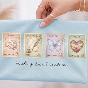 May include: A light blue fabric with four postage stamp designs. The stamps feature a brain, journal page, butterfly, and heart, each with a price. The text "Healing. Don't rush me." is below the stamps.