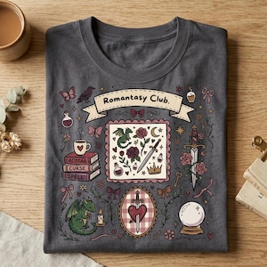 May include: A charcoal gray t-shirt featuring a graphic print with the text "Romantasy Club." The design includes illustrations of a dragon, a sword, roses, a stack of books labeled "ACOTAR," "CURSE," and "SPELL," a crystal ball, and bows.