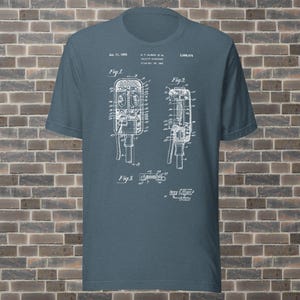 May include: Blue t-shirt featuring a white schematic diagram of a vintage microphone. The diagram includes detailed technical drawings and text, including the date "Jan. 11, 1955". The shirt is made of a soft material.