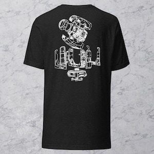 May include: Black t-shirt featuring a white schematic design of a mechanical device. The graphic shows detailed internal components, including gears, housings, and other parts. The design is centered on the back of the shirt.