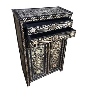Peut inclure: Armoire décorative noire et blanche avec deux tiroirs ouverts. L'armoire présente des motifs géométriques et floraux complexes. L'armoire a deux portes avec du matériel décoratif. L'armoire est en bois.