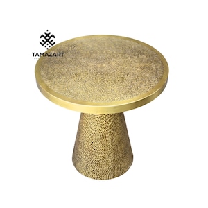 May include: A brass-coloured side table with an etched pattern on the circular tabletop. The table has a cone-shaped base with a hammered texture. The table is a decorative accent piece, suitable for a living room or hallway.