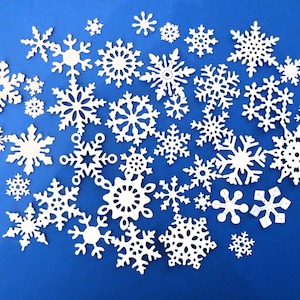 May include: A collection of white paper snowflakes of various sizes and designs scattered on a blue background. The snowflakes have intricate cut-out patterns, creating a delicate and festive appearance. Ideal for winter-themed crafts and decorations.