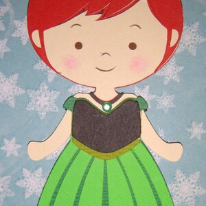 K&ouml;nnte beinhalten: Eine Papierpuppe einer jungen Frau mit roten Haaren, die ein gr&uuml;nes Kleid mit schwarzem Oberteil und gr&uuml;nen Edelsteinen tr&auml;gt. Die Puppe befindet sich auf einem blauen Hintergrund mit wei&szlig;en Schneeflocken.
