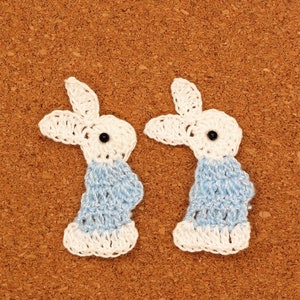 May include: Two crocheted bunny rabbit shapes with white and light blue yarn. The bunnies have black button eyes.