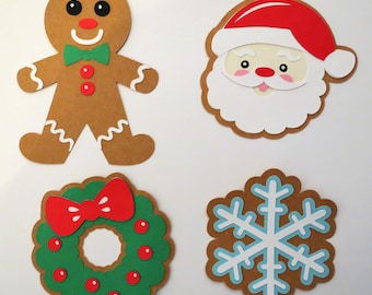 May include: Four festive paper cutouts: a gingerbread person, Santa Claus, a snowflake, and a wreath with a red bow. The gingerbread person is brown with white icing details, Santa is red and white, the snowflake is blue and white, and the wreath is green with red berries and a red bow.