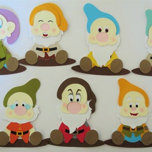 May include: Seven paper cutouts of the seven dwarfs from the Disney movie Snow White. Each dwarf is sitting down with brown legs and a brown base. The dwarfs are wearing different colored hats and shirts.