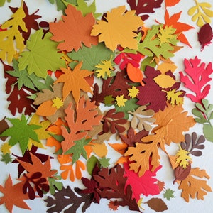 May include: A collection of colorful paper leaves in various shapes and sizes. The leaves are in shades of orange, red, brown, yellow, and green, creating a fall-themed arrangement. Some leaves have intricate details, while others are simpler.