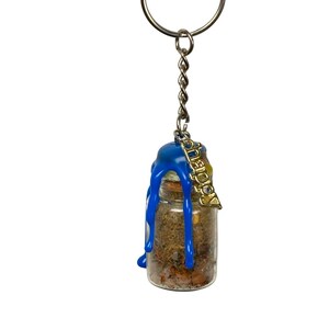 May include: A small glass bottle filled with herbs and spices, sealed with a cork and blue wax. A silver keyring holds the bottle, with a gold-coloured charm that reads "DEITY".