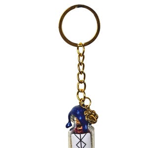 May include: A gold-coloured keyring with a small glass bottle charm. The bottle has a blue cap and a paw print charm. The bottle has a white label with a symbol and the word "protection".