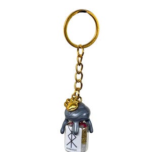 May include: A gold-coloured keyring with a small glass bottle pendant. The bottle is filled with herbs and has a grey, dripped-wax-like top. A gold paw print charm hangs above the bottle. The bottle has the word "Protection" and a symbol.