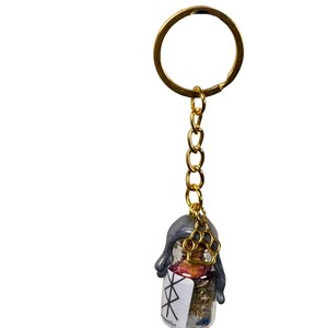 May include: A gold-coloured keyring with a small glass bottle pendant. The bottle contains dried herbs and flowers, sealed with grey wax and a gold paw charm. The bottle has a white label with black symbols.
