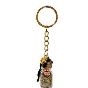 May include: A miniature glass bottle keyring filled with dried herbs and crystals. The bottle is sealed with a cork and adorned with a gold-coloured paw print charm. A gold chain and keyring complete the design.
