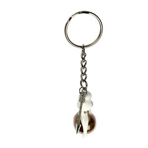 May include: A silver keychain with a small glass vial containing a brown substance and a white figurine pierced by a silver arrow. The keychain has a silver ring and chain.