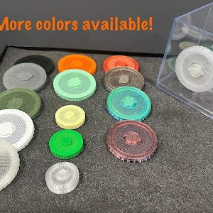 May include: A collection of colorful, circular objects with a mesh-like design, displayed on a dark surface. The objects come in various colors, including orange, green, and gray. The text "More colors available!" is visible in the image.