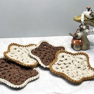 May include: Four star-shaped crochet coasters in alternating dark brown and cream colors. A decorative mushroom-shaped figurine with two small bird figures sits nearby, adorned with a white beaded bracelet featuring silver-toned accents.