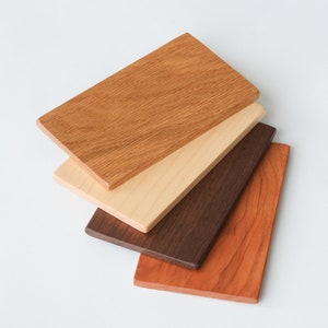 May include: Four wood samples in different colors and grain patterns. The samples are arranged in a stack, with the lightest wood on top and the darkest wood on the bottom. The wood samples are all rectangular in shape.