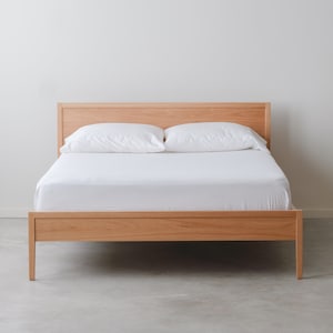 May include: A wooden bed frame with a white mattress and two white pillows. The bed frame is made of light wood and has a simple design.