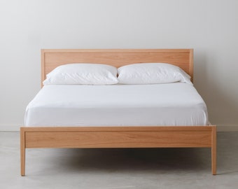 May include: A wooden bed frame with a white mattress and two white pillows. The bed frame is made of light wood and has a simple design.