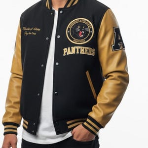 May include: Black and tan varsity jacket with a round patch featuring a panther and the word "PANTHERS". The jacket has tan leather sleeves, a black body, and gold and black striped trim on the cuffs and collar. An "A" is on the right sleeve.