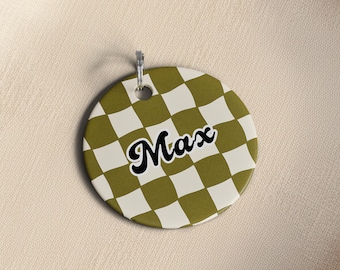 May include: A round, olive green and white checkered tag with the name "Max" in black script. The tag has a silver metal loop for hanging.