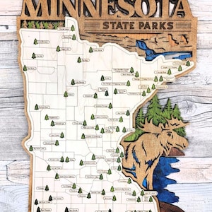 May include: Wooden map of Minnesota State Parks. The map is laser-cut with a light wood finish and features the state outline, park names, and a moose illustration. The text "MINNESOTA STATE PARKS" is at the top.