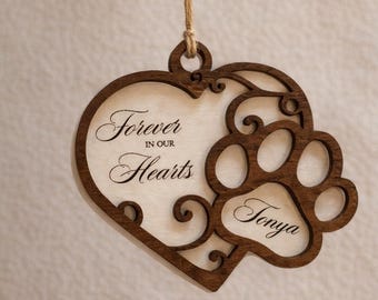 May include: Wooden heart-shaped ornament with a paw print design. The ornament has the words "Forever in our Hearts" and the name "Tonya" engraved. It is suspended by a natural twine string.