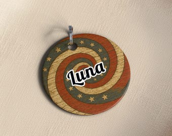 May include: A round wooden tag with a spiral design in red, beige, and green, adorned with gold stars. The word "Luna" is written in white script across the center. A silver metal ring is attached at the top.