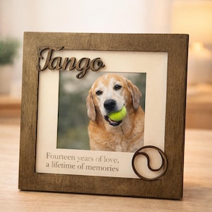 May include: Wooden photo frame with the name "Tango" in script. The frame holds a photo of a dog with a tennis ball in its mouth. The text "Fourteen years of love, a lifetime of memories" is printed below the photo. A decorative swirl is on the lower right corner.