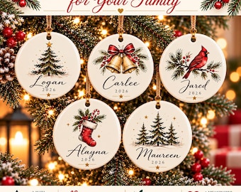 May include: Five round white ceramic Christmas ornaments featuring festive illustrations of a tree, bells, a cardinal, a stocking, and a forest. Each ornament is personalized with a name and the year 2026, hanging by gold strings on a tree.