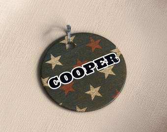 May include: A round, wooden keychain with a distressed, star-patterned design in shades of blue, brown, and beige. The name "COOPER" is printed in bold, white letters with a black outline. A silver-colored metal ring is attached at the top.