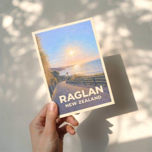 May include: A postcard depicting a coastal scene in Raglan, New Zealand, with a pathway leading to the sea under a bright sun. The text "RAGLAN NEW ZEALAND" is displayed in white.