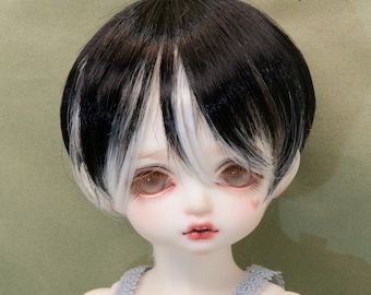 May include: A doll with short black and white hair wearing a white lace dress with blue straps and a beaded embellishment.