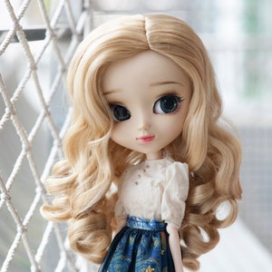 May include: A doll with long blonde curly hair wearing a white blouse and a blue and gold skirt with stars. The doll has blue eyes and a painted smile.