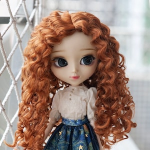 May include: A doll with auburn curly hair, large blue eyes, and a fair complexion. The doll wears a white blouse with small buttons and a blue skirt with a starry night design. The skirt has a black lace trim.