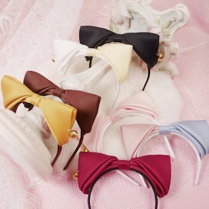 Può includere: Assortimento di fasce per capelli con orecchie di gatto colorate con fiocchi. Ogni fascia presenta un fiocco di colore diverso, tra cui bianco, nero, giallo, marrone, rosa, blu e bordeaux.