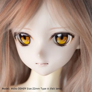May include: Close-up of a doll's face with yellow eyes. The doll has light brown hair and is wearing a light pink lip color. The caption below the image reads "Model: Volks-DDH09 Size: 22mm Type A (falt lens)".