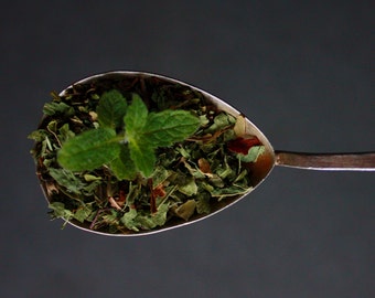 May include: A silver spoon filled with a blend of dried herbs and a sprig of fresh mint.