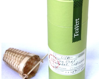 May include: A green cardboard tube with a white label that says "TeaVert" and "USA Tea Vert Herbal Infusion". The tube has a green and white label with the text "Hand Packed" and "TeaVert". A bamboo tea infuser is in the foreground.