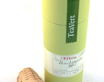 May include: A green cylindrical tube with a label that reads "TeaVert - Loose Leaf Tea" and "Ceylon -  Sencha OP1". The tube is sitting on a white surface next to a bamboo tea infuser.