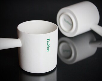 May include: Two white ceramic teacups with handles. The cup on the left has the word "TeaVert" printed on the side in green lettering.