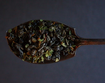 May include: A silver spoon filled with loose leaf green tea. The tea is a blend of green tea leaves, herbs, and flowers.