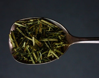 May include: A silver spoon filled with loose green tea leaves.