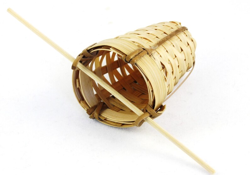 May include: A woven bamboo tea infuser with a wooden handle. The infuser is cylindrical and has a woven pattern. The handle is attached to the infuser at the top and bottom.