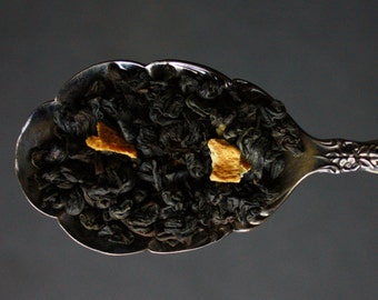 May include: A silver spoon filled with black tea leaves and orange peel pieces.