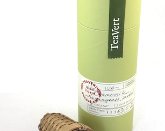 May include: A green cardboard tube with a label that reads "TeaVert - Loose Leaf Tea" and "USA" with a red stamp that reads "Hand Packed" and "Organic". The tube is next to a small brown bamboo tea infuser.
