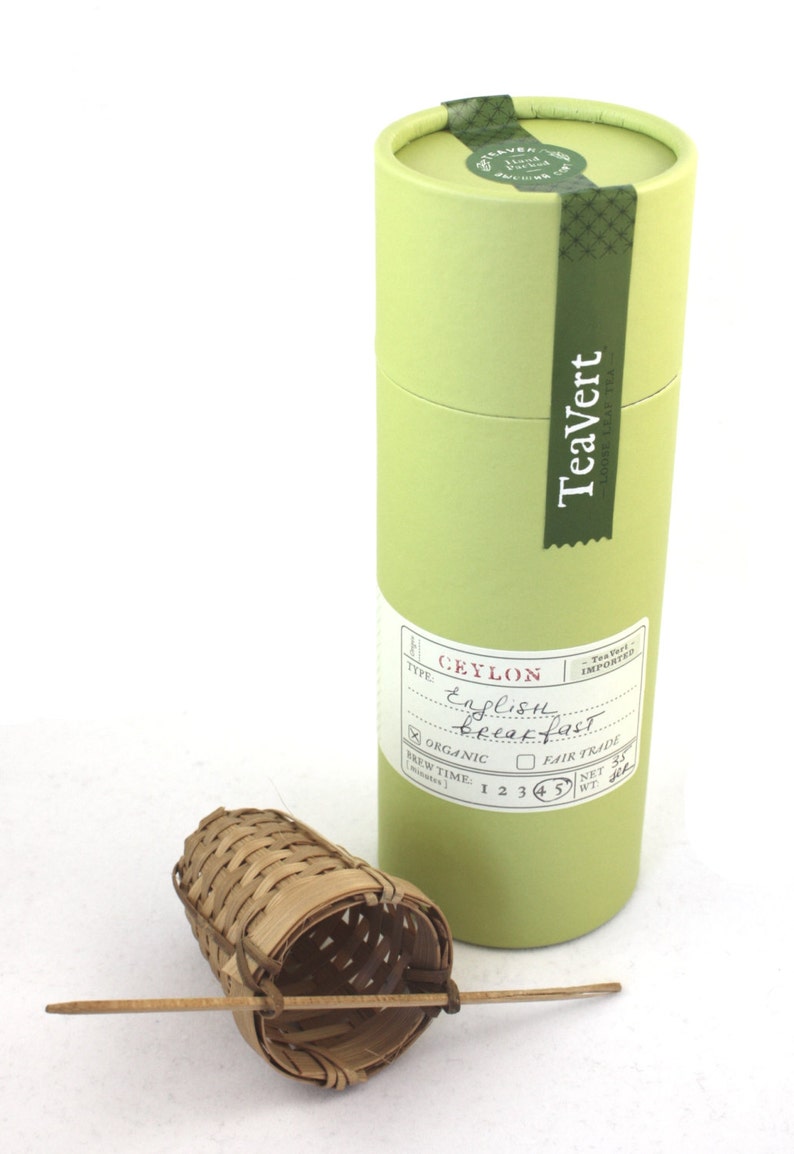 May include: A green cylindrical box with a white label that reads "TeaVert - Ceylon English Breakfast - Organic - Fair Trade - Net Wt. 31g" and a bamboo tea infuser with a wooden handle.