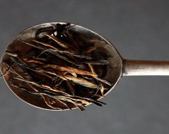 May include: A silver spoon filled with loose leaf tea. The tea is a mix of black and brown tea leaves.