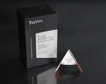 May include: A black box with white text that reads "TeaVert. Premium PU-ERH TEA COLLECTION 1992 Aged Organic Jing Mai Green Sheng NET WT 1.6 OZ (45g)". A silver tea bag is in the foreground.
