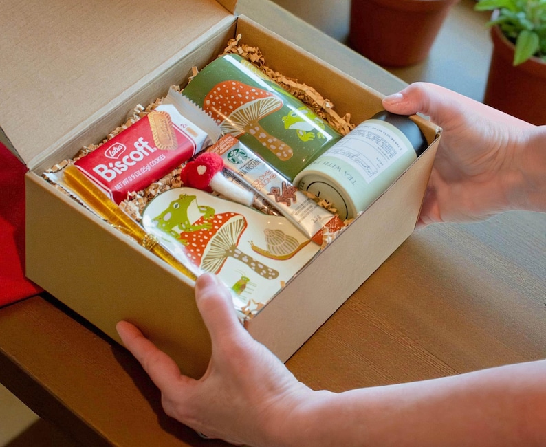 Hands opening the Frog Mushroom Mug Gift Box revealing neatly packed cozy contents designed for heartfelt gifting and woodland themed joy perfect for birthdays self care or thoughtful Christmas presents for nature lovers